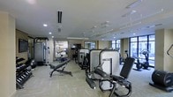 This fitness center offers a thorough and well-organized workout environment designed to accommodate a wide range of exercise needs. The space is outfitted with a robust selection of professional-grade strength training machines and cardiovascular equipment, including cable machines, weight benches, treadmills, and various resistance stations, providing users with everything needed for a complete workout routine.

The interior features a clean, neutral color palette with light-toned walls and flooring that create a bright, open atmosphere. Recessed lighting is evenly distributed across the ceiling, ensuring consistent illumination throughout the space, while large windows along one wall invite ample natural light and offer views to the exterior. Large wall-mounted mirrors are strategically placed to enhance the sense of depth and allow users to monitor their form during exercise.

The layout is thoughtfully arranged to maximize usable floor space while maintaining clear pathways between equipment. A mounted flat-screen television is also present, adding a convenient entertainment option for users during their workouts. Overall, the fitness center presents a clean, professional, and functional environment suitable for a variety of fitness levels and training goals.