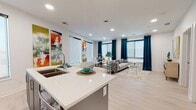 This contemporary apartment showcases a harmonious blend of style and functionality. The open-concept living area is adorned with a plush tufted sofa, sleek glass coffee table, and eye-catching abstract artwork. Large windows with teal curtains allow ample natural light, enhancing the airy feel of the space. The kitchen boasts modern appliances, white cabinetry, and a convenient island with seating. Light wood-look flooring unifies the living spaces, while recessed lighting provides a warm ambiance throughout.

The bedroom features a bold color scheme with vibrant red accents against neutral tones. A striking forest-themed artwork serves as a focal point above the bed. The bathroom continues the contemporary theme with clean lines, a glass-enclosed shower, and modern fixtures. Attention to detail is evident in the carefully curated decor and furnishings, creating a cohesive and inviting atmosphere throughout the apartment. This space exemplifies urban living with its blend of comfort, style, and practical design.