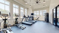 Located at 4275 Valley St in Enola, PA, this fitness center offers a well-appointed, single-room workout space designed to support a full range of exercise routines. The room features vaulted ceilings that lend an open, airy atmosphere, accentuated by large multi-pane windows lining the walls and flooding the space with abundant natural light and views of the surrounding community. Durable, dark rubber flooring provides a practical and resilient surface throughout.

The cardio section is well-stocked with multiple treadmills, elliptical trainers, and stationary bikes, complemented by wall-mounted flat-screen TVs for entertainment during workouts. A dumbbell rack and adjustable weight bench round out the free weights area, while a cable machine offers versatile strength training options. Overhead, industrial-style pendant lights and a large ceiling fan contribute to both the aesthetic and comfort of the space.

Stylish navy-framed glass double doors serve as the main entry, adding a modern architectural touch. A bold motivational wall graphic reading "YOUR ONLY LIMIT IS YOU." sets an energizing tone. Recessed lighting and clean white walls complete the bright, contemporary feel, making this fitness center a functional and inviting space for residents to pursue their wellness goals.