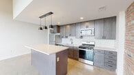 Located on the 8th floor of 20 S Ontario St in downtown Toledo, Ohio, this one-bedroom, one-bathroom unit blends industrial character with contemporary finishes throughout its well-proportioned layout. The open living and kitchen area is anchored by polished concrete floors that reflect natural light, while an exposed brick accent wall adds raw, architectural texture. Soaring ceilings amplify the sense of volume in the main living space, which benefits from large, grid-pane windows offering elevated views of the surrounding cityscape.

The kitchen is thoughtfully designed with dark-toned shaker cabinetry, a white quartz countertop island with pendant lighting above, stainless steel appliances including a gas range and refrigerator, and a subway tile backsplash. The layout provides practical workspace and storage.

The bedroom features soft carpeting, tall ceilings, and an exposed brick wall that carries the building's industrial aesthetic into the private space. A walk-in closet offers organized storage. The bathroom is clean and modern, with polished concrete floors continuing the unit's material palette, a dark-vanity with a white basin, a full soaking tub with shower, and a classic sconce-lit mirror. A hallway connects the private spaces to the main living area.