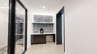 This amenity space in Revere, MA offers a comprehensive suite of facilities designed to support both fitness and productivity. The layout is anchored by two dedicated exercise rooms that together create a full-featured fitness center. Floor-to-ceiling windows flood the workout areas with natural light and provide open views of the surrounding outdoors, enhancing the sense of space. The fitness rooms are outfitted with cardio equipment — including treadmills, ellipticals, and stationary bikes — as well as a strength training area featuring free weights, weight racks, benches, and a cable machine. Cushioned exercise mats cover portions of the floor, providing a dedicated space for stretching and functional training. The ceilings feature a deep navy acoustic tile finish with sleek linear lighting, lending a modern, polished aesthetic throughout. A conference and dining room provides a refined gathering space, highlighted by a textured, artistic wall mural and a wall-mounted display screen above a clean, light-wood conference table surrounded by ergonomic seating. A private office rounds out the suite, offering a quieter workspace. Connecting hallways tie all areas together efficiently, making for a seamless and well-organized amenity floor.