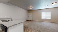 This two-story home is designed with a practical, neutral aesthetic that provides a clean and versatile living environment. The main level opens to a spacious living area finished with plush carpet and wood-look luxury vinyl plank flooring, with a clear transition between zones. A peninsula-style kitchen anchors the space, featuring granite-look countertops, white cabinetry, a built-in sink, and black appliances including a refrigerator, microwave, and range. The kitchen overlooks the living area, creating an open and connected layout. A front entry door with a small foyer mat provides a defined arrival point, while a window fitted with blinds allows natural light into the main living space. The textured ceiling and flush-mount lighting are consistent throughout the lower level.

The upper floor, accessible via a staircase visible in the 3D model, contains additional rooms with carpeted flooring and wood-look hallway transitions. Multiple white panel doors lead to various spaces, including generously sized walk-in closets outfitted with double hanging rods and built-in shelving. A full bathroom on this level includes a tub-shower combo, white cabinetry with granite-look counters, and tile flooring. A separate water closet with wood-look flooring provides added privacy.