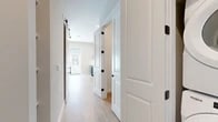 This efficiently designed single-floor, one-bedroom, one-bathroom unit makes excellent use of its compact footprint. Light oak-toned luxury vinyl plank flooring runs throughout, creating a cohesive and contemporary aesthetic. The open-concept kitchen and dining area is a standout feature, showcasing two-tone cabinetry — white uppers paired with bold navy lowers — accented by gold hardware, a herringbone tile backsplash, stainless steel appliances including a full-size refrigerator and dishwasher, and recessed lighting overhead. A sliding barn door with matte black hardware adds a stylish design element at the kitchen entry. The living room benefits from abundant natural light courtesy of large windows and a glass-panel exterior door that opens to the outdoors, while a ceiling fan enhances comfort. A central hallway, lined with panel-style doors featuring matte black hardware, connects the rooms and provides access to two closets and an in-unit laundry area. The bedroom offers a private and cozy retreat. The bathroom features warm wood-toned flooring, white shaker-style cabinetry with gold pulls, a large illuminated mirror, and matte black bar hardware. The overall palette of soft neutrals and crisp white trim lends the space a clean, modern character throughout.