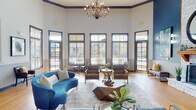 Located at 1 Springtime Blvd SW in Huntsville, Alabama, this single-story community clubhouse offers a thoughtfully designed gathering space defined by soaring ceilings, rich hardwood flooring, and a cohesive blue-and-white color palette throughout. The expansive main lounge serves as the heart of the facility, anchored by a striking white stone fireplace with a warm wood mantel, an oversized round mirror, and an elegant multi-arm chandelier that adds a refined focal point overhead. Exposed wood beam accents and tall, dark-trimmed windows flood the space with natural light while offering views of the surrounding outdoor area, including a pool. A co-working and business lounge provides reclaimed wood communal tables, computer workstations, a whiteboard, and seating nooks with chartreuse velvet accent chairs — ideal for productive work sessions. The full galley kitchen features rich wood cabinetry, granite countertops, tile flooring, and full appliances to support resident events and gatherings. Curated abstract artwork is displayed throughout, enhancing the modern yet inviting ambiance. A dedicated fitness center is also accessible directly from the main lounge. Throughout the space, beadboard wainscoting, crown molding, and consistent design details create a polished and cohesive aesthetic.