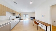 Located at 399 S Crouse Ave in Syracuse, NY, this thoughtfully designed single-floor unit offers a clean, contemporary aesthetic throughout. The open layout is anchored by warm light wood flooring that runs seamlessly across the living and kitchen areas, enhancing the sense of spaciousness and continuity.

The kitchen is a standout feature, outfitted with a full suite of stainless steel appliances including a refrigerator, electric range, over-the-range microwave, and dishwasher. Two-tone cabinetry — natural wood upper cabinets paired with crisp white lower cabinets — frames clean white countertops, creating a modern yet warm workspace. A large window floods the kitchen and living area with abundant natural light while offering views of the building's exterior corridor and surroundings.

The bathroom is finished with the same light wood-style flooring and features bright white walls, a toilet, and practical grab bars, indicating accessibility-conscious design. The space is clean and functional.

The dedicated closet is equipped with a versatile wire shelving and hanging rod system, providing organized storage across multiple tiers. The overall ambiance of the unit is bright, minimal, and modern, making it a well-structured and functional living space in the heart of Syracuse.