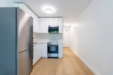 Located at 289 Niagara St in Toronto's vibrant King West neighbourhood, this efficiently designed unit makes excellent use of its compact footprint across a single floor. Light-toned hardwood flooring runs throughout, lending a clean, cohesive warmth to the entire space.

Upon entry, a narrow hallway with an electrical panel leads into the heart of the unit. The main living area is bright and open, featuring a large window that frames a leafy outdoor view and allows generous natural light to fill the room. A wall-mounted air conditioning unit and baseboard heating ensure year-round comfort.

The kitchen is thoughtfully appointed with a modern, minimalist aesthetic. Crisp white flat-front cabinetry extends from countertop to ceiling, maximizing storage. Stainless steel appliances — including a full-height refrigerator, electric range, microwave, and undermount sink with a contemporary faucet — complete the functional and stylish cooking space.

The bathroom features a walk-in shower with full white square-tile surround, mosaic tile flooring, and chrome fixtures, presenting a clean and practical design. Throughout the unit, the consistent use of white walls, bright finishes, and natural wood flooring creates a fresh, contemporary ambiance well-suited to urban living in Toronto.