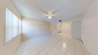 This single-floor residence offers a clean, functional layout designed for comfortable everyday living. Light-colored ceramic tile flooring runs consistently throughout the entire space, creating a cohesive and easy-to-maintain interior. A long central hallway connects the main living areas, providing clear and efficient circulation between rooms.

The kitchen is efficiently designed, featuring white cabinetry, a full-size refrigerator, an electric range, and a built-in sink with overhead cabinets for storage. A textured ceiling with recessed lighting keeps the kitchen well-lit. Adjacent to the kitchen is an open living or dining area, also finished with the same tile flooring and illuminated by a flush-mount ceiling light.

The bedrooms are generously proportioned, each equipped with ceiling fans for air circulation and louvered bifold closet doors providing ample storage. One bedroom features a window with vertical blinds, allowing natural light to filter into the room.

The bathroom is straightforward and functional, featuring a single vanity with a sink, a wall-mounted mirror with overhead lighting, and a combined bathtub and shower enclosure with white tile surround. The overall palette of the space is neutral and bright, with cream-toned walls and white trim throughout, contributing to an airy and open ambiance.