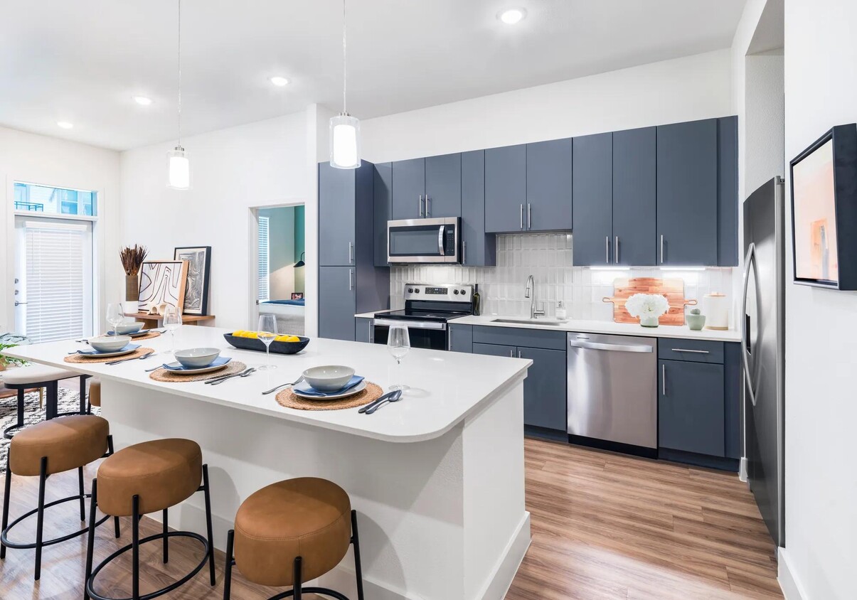 Indulge in culinary delights within Modera Garden Oaks' gourmet kitchens, highlighted by quartz countertops and custom 42-inch cabinetry featuring under-cabinet lighting for both style and practicality. - Modera Garden Oaks