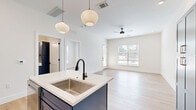 Located in Frisco, TX, this thoughtfully designed one-bedroom, one-bathroom unit delivers a modern aesthetic with high-quality finishes throughout. The open-concept kitchen and living area serves as the heart of the home, anchored by a striking kitchen outfitted with bold navy blue shaker cabinets, gold hardware, a marble-look tile backsplash, white quartz countertops, and a central island with an undermount sink. Stainless steel appliances, including a French door refrigerator, electric range with microwave, and dishwasher, complete the culinary space. Pendant globe lights hang above the island, adding a contemporary touch. Light-toned hardwood flooring flows seamlessly throughout, brightening the entire unit. The living area is spacious and airy, featuring a ceiling fan, recessed lighting, and a private entry door alongside a large window that invites abundant natural light. The bedroom is well-proportioned, offering dual windows with outdoor views and ample natural light, complemented by a dedicated closet. The bathroom is a design highlight, showcasing a bold geometric mosaic tile surround in the tub/shower, a blue vanity with gold hardware, matte black fixtures, and grey floor tile — a cohesive and stylish finish to this well-appointed space.