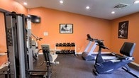 Located at 2408 Duck Pond Cir in Morrisville, NC, this dedicated fitness center offers a focused and functional workout environment designed to meet a variety of exercise needs. The space is housed on a single floor and immediately draws attention with its bold orange accent walls, which lend an energetic and motivating atmosphere to the room. Recessed lighting illuminates the space evenly, ensuring a bright and comfortable environment during any workout session. The flooring consists of durable rubber matting, providing both safety and shock absorption for high-impact activities. The fitness area is well-equipped with a treadmill and additional cardio equipment, making it suitable for endurance training. A full dumbbell rack stocked with multiple weight sets serves the free weights section, catering to strength training routines of varying intensity. A dedicated strength machine is also present, offering targeted muscle training options. A wall-mounted flat-screen television adds an entertainment element, allowing users to stay engaged during longer workouts. Framed athletic artwork adorns the walls, reinforcing the fitness-focused ambiance of the space. Compact yet thoughtfully organized, this fitness center provides a comprehensive and inviting workout facility.