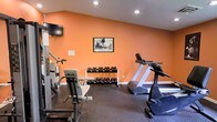 Located at 2408 Duck Pond Cir in Morrisville, NC, this dedicated fitness center offers a focused and functional workout environment designed to meet a variety of exercise needs. The space is housed on a single floor and immediately draws attention with its bold orange accent walls, which lend an energetic and motivating atmosphere to the room. Recessed lighting illuminates the space evenly, ensuring a bright and comfortable environment during any workout session. The flooring consists of durable rubber matting, providing both safety and shock absorption for high-impact activities. The fitness area is well-equipped with a treadmill and additional cardio equipment, making it suitable for endurance training. A full dumbbell rack stocked with multiple weight sets serves the free weights section, catering to strength training routines of varying intensity. A dedicated strength machine is also present, offering targeted muscle training options. A wall-mounted flat-screen television adds an entertainment element, allowing users to stay engaged during longer workouts. Framed athletic artwork adorns the walls, reinforcing the fitness-focused ambiance of the space. Compact yet thoughtfully organized, this fitness center provides a comprehensive and inviting workout facility.