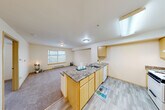 Located at 13000 Linden Ave N in Seattle, WA, this one-bedroom, one-bathroom unit offers a thoughtfully arranged floor plan that maximizes every square foot. The open-concept layout connects the kitchen and living area seamlessly, creating a functional and welcoming common space. The kitchen is equipped with light maple cabinetry, a granite-style peninsula countertop with a built-in sink, a white appliance suite including a refrigerator, electric range, and dishwasher, and durable wood-look flooring. A skylight above the kitchen area brings in additional natural light, brightening the space considerably. The living area features neutral carpet, a baseboard heater, and a window that frames views of the surrounding Seattle landscape. The bedroom is carpeted and includes a closet, a window with blinds, and easy access to the rest of the unit. Three closets throughout the unit provide ample storage. The bathroom features a full tub-shower combination. Neutral warm tones on the walls and ceilings throughout lend the unit a clean, consistent aesthetic well-suited for comfortable everyday living in the Linden neighborhood of North Seattle.
