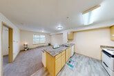 Located at 13000 Linden Ave N in Seattle, WA, this one-bedroom, one-bathroom unit offers a thoughtfully arranged floor plan that maximizes every square foot. The open-concept layout connects the kitchen and living area seamlessly, creating a functional and welcoming common space. The kitchen is equipped with light maple cabinetry, a granite-style peninsula countertop with a built-in sink, a white appliance suite including a refrigerator, electric range, and dishwasher, and durable wood-look flooring. A skylight above the kitchen area brings in additional natural light, brightening the space considerably. The living area features neutral carpet, a baseboard heater, and a window that frames views of the surrounding Seattle landscape. The bedroom is carpeted and includes a closet, a window with blinds, and easy access to the rest of the unit. Three closets throughout the unit provide ample storage. The bathroom features a full tub-shower combination. Neutral warm tones on the walls and ceilings throughout lend the unit a clean, consistent aesthetic well-suited for comfortable everyday living in the Linden neighborhood of North Seattle.