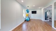 Located in Cape Coral, Florida, this single-story fitness facility offers a comprehensive workout environment thoughtfully designed for a range of exercise activities. The space is divided into two distinct areas: a generously sized exercise room and a flexible multipurpose living/studio room.

The main exercise room features light-toned carpet flooring, crown molding, and soft blue-gray walls that create a clean, motivating atmosphere. Recessed lighting illuminates the space evenly, complemented by multiple windows that invite natural light and views of the surrounding exterior. The room is outfitted with an extensive array of Matrix-brand strength machines, cable systems, free-weight benches, a dumbbell rack, multiple treadmills, elliptical trainers, a recumbent bike, and a rowing machine. Wall-mounted flat-screen televisions are positioned throughout for entertainment during workouts. A large mirror wall expands the sense of space and supports strength training.

The adjoining studio room features warm hardwood-style flooring and floor-to-ceiling mirrors along one wall, making it ideal for group fitness, yoga, or stretching sessions. Exercise balls, rollers, and accessories are neatly organized within the room. Natural light filters in through windows, and a wall-mounted television adds versatility. Double glass doors connect the main exercise room to an outdoor area, enhancing the open, airy feel of the entire facility.