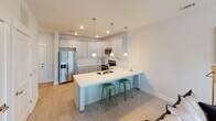 This single-floor residence in Fort Mill, SC offers a thoughtfully designed layout that prioritizes functionality and a cohesive aesthetic. The open-concept kitchen serves as a centerpiece of the living area, featuring gray shaker-style cabinetry with brushed nickel hardware, white quartz countertops, and a full suite of stainless steel appliances including a French door refrigerator, electric range with over-the-range microwave, and dishwasher. A peninsula with an undermount double sink extends the counter space and provides seating for multiple bar stools, with pendant lighting suspended above to define the zone. Recessed lighting throughout the kitchen ensures bright, even illumination.

The living area transitions seamlessly from the kitchen, finished with light wood-look flooring and neutral walls that create a calm, versatile backdrop. The bedroom is carpeted and generously sized, receiving natural light through dual windows with blinds. A ceiling fan adds comfort, and the room connects to a dedicated bathroom featuring a marble-style quartz vanity top, an undermount sink, and a large mirror with overhead lighting. The overall palette of soft whites, grays, and warm neutrals lends the space a clean, modern character throughout.
