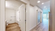 Located at 18807 8th Ave NE in Shoreline, Washington, this thoughtfully designed single-floor unit offers an efficient and modern living experience. Light hardwood flooring runs throughout the entire space, creating a warm and cohesive aesthetic from room to room.

The combined kitchen and living area forms the heart of the unit. The kitchen is outfitted with stainless steel appliances — including an electric range, over-the-range microwave, and dishwasher — complemented by gray lower cabinets, warm wood-toned upper cabinetry, light quartz countertops, and a subway tile backsplash. Recessed lighting and a practical layout make this kitchen both functional and visually appealing.

The living area is bright and open, featuring a ceiling fan with light fixture and a sliding glass door that opens onto a private balcony with views of the surrounding tree canopy — allowing for ample natural light and a pleasant outdoor connection.

A hallway connects the living spaces to the bathroom, which features gray cabinetry with a vanity sink, a toilet, grab bars, and a shower/tub combination. Wire shelving in the adjacent closet area provides organized storage. A sliding frosted-glass barn door adds a modern design touch to the hallway, enhancing the contemporary character of the unit.