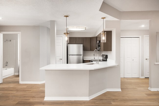 Modern apartment kitchen with elegant white countertops, stainless steel appliances, and warm wood flooring. - Avana Belmar