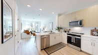 Located at 100 Avenue G in Bayonne, NJ, this thoughtfully designed two-bedroom, one-bathroom residence offers a bright and modern living experience across a single, well-organized floor. The open-concept layout seamlessly connects the kitchen and living room, creating an inviting, functional space ideal for everyday living and entertaining. The contemporary kitchen is a standout feature, showcasing a mix of white and light wood cabinetry, white subway tile backsplash, stainless steel appliances including a range, microwave, dishwasher, and refrigerator, and a peninsula with bar seating and a clean white countertop. Light hardwood-style flooring runs throughout the main living areas, enhancing the bright, airy ambiance. The living room benefits from large windows that draw in generous natural light, creating a warm and welcoming atmosphere. The primary bedroom is a comfortable retreat, featuring a sizable window with exterior views, light neutral walls, and ample space. A second bedroom offers additional flexibility. The shared bathroom is finished with large-format light tile flooring, a soaking tub with tiled surround, and a wood-toned vanity. The entry hallway provides a clean transition into the home, with recessed lighting carried throughout the unit for a polished, cohesive look.