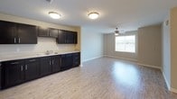 This thoughtfully laid-out one-bedroom, one-bathroom residence spans a single floor and features a clean, modern aesthetic throughout. The open living area is finished with light-toned hardwood-style flooring and neutral walls, creating a bright and welcoming atmosphere. Flush-mount ceiling fixtures provide consistent lighting, while a ceiling fan in the living area adds comfort and airflow. Ample closet space is conveniently located near the entryway, offering excellent storage options. The kitchen is well-appointed with dark espresso cabinetry, light countertops, and a full suite of black appliances including a refrigerator, range, built-in microwave, and dishwasher. The L-shaped layout maximizes counter and cabinet space, making the kitchen both functional and efficient. The bedroom is carpeted for comfort and features a ceiling fan with a light kit, a window that invites natural light, and a dedicated closet with built-in shelving. The bathroom is finished with beige tile flooring, a dark vanity with a white countertop, and a full tub-shower combination. The cohesive use of contrasting dark cabinetry against light surfaces throughout the unit lends a polished, contemporary feel to the overall space.
