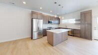 Located at 2242 E Brookings Dr in Draper, UT, this contemporary three-bedroom, two-bathroom home spans three floors, offering a well-organized and functional layout. Light hardwood flooring flows consistently throughout the interior, complementing the crisp white walls and clean modern aesthetic.

The main living level features an open-concept kitchen and living room, filled with natural light from large windows with blinds. The kitchen is well-appointed with warm taupe shaker-style cabinetry, white quartz countertops, a central island with pendant lighting, and a full suite of stainless steel appliances including a refrigerator, range, microwave, and dishwasher.

The bedrooms are bright and airy, with tall ceilings and generously sized windows that frame outdoor views of the surrounding Draper landscape. The primary bedroom offers a comfortable and private retreat. The two bathrooms are finished with the same taupe cabinetry and white quartz vanities. One bathroom features a soaking tub with tiled surround, while the other includes a glass-enclosed walk-in shower.

Two stairways connect the three floors, with hallways providing smooth circulation between spaces. The ground floor includes a spacious two-car garage with an automatic opener and overhead lighting, adding practical storage and parking utility to the home.