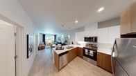 This thoughtfully designed single-floor residence offers a seamless blend of modern aesthetics and functional living. The open-concept layout connects the kitchen and living area, creating an inviting, airy atmosphere. The kitchen is outfitted with two-tone cabinetry — warm wood lower cabinets paired with crisp white upper cabinets — complemented by light quartz countertops, a peninsula with a double sink, and a full suite of stainless steel appliances including a refrigerator, range, microwave, and dishwasher. Light hardwood-style flooring runs throughout, reinforcing the space's clean, contemporary feel. The living area is bright and comfortable, anchored by a large window that frames views of lush outdoor greenery, allowing generous natural light to fill the room. The bedroom continues the modern palette with light walls, hardwood-style flooring, and a sizable window offering serene outdoor views and natural light. The bathroom features a full tub-shower combination, a wide vanity with an undermount sink, a large mirror, and neutral tile flooring, delivering a clean and practical design. Throughout the residence, the consistent use of light tones, recessed lighting, and quality finishes create a cohesive and welcoming environment.