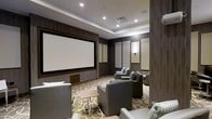 Located at 201 Willett Ave in Port Chester, New York, this private screening room delivers an immersive cinematic experience within a refined, thoughtfully designed space. The room is anchored by a large, wall-mounted projection screen framed by sleek wood-paneled surrounds, creating a true theater-like focal point. Recessed ceiling lighting provides a soft, ambient glow, complemented by subtle wall sconces that add warmth without detracting from the viewing experience. The walls are fitted with acoustic panels, ensuring excellent sound quality and minimizing unwanted reverberation for an optimal audio environment. Plush, generously sized gray armchairs are arranged in a tiered layout across a stylishly patterned carpet, offering clear sightlines to the screen from every seat. Small side tables are conveniently positioned between chairs, adding practical functionality to the space. The tray ceiling adds an architectural element of elegance, enhancing the room's sense of depth and refinement. The overall ambiance is one of upscale comfort and sophistication, making this screening room an ideal venue for private film viewings, presentations, or entertainment gatherings.