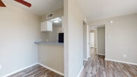 This single-floor unit offers a functional and cohesive layout with wood-style plank flooring extending consistently throughout every room, lending a warm, unified aesthetic to the space. The living area serves as the central hub, featuring a ceiling fan with integrated lighting and a full-width sliding glass door dressed with vertical blinds, allowing abundant natural light and outdoor views to pour in.

The galley-style kitchen is efficiently designed with white cabinetry, a blue-toned laminate countertop, a stainless steel sink, and black appliances including a refrigerator and electric range. A pass-through counter with overhead cabinetry connects the kitchen to the adjacent living and dining area, enhancing the open feel between spaces.

A hallway leads to the private areas of the unit, including bedrooms equipped with ceiling fans and windows fitted with horizontal blinds for light control and privacy. One bedroom features a large window that brings in generous natural light.

The bathroom is outfitted with a single-sink vanity featuring a blue laminate countertop, a dark-framed mirror with overhead lighting, white cabinetry, and a tub-shower combination. Neutral beige tones on the walls complement the flooring throughout, creating a clean and consistent overall ambiance.