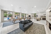 Located at 28850 Mission Blvd in Hayward, CA, this single-floor clubhouse offers a well-appointed communal space designed for both relaxation and social gatherings. The interior is finished with large-format white tile flooring throughout, recessed lighting, and a neutral color palette that creates a clean, contemporary atmosphere.

The kitchen is fully equipped with stainless steel appliances, dark cabinetry, a mosaic tile backsplash, and a wall-mounted range hood. A generous peninsula with a quartz-style countertop and bar-height seating provides an inviting casual dining setup. Large floor-to-ceiling windows flood the kitchen with natural light and offer views of the outdoor courtyard.

The dining area features multiple round pedestal tables with swivel bar stools, positioned near expansive windows and sliding glass doors that open directly to a pool and pergola area outside. A wall-mounted flat-screen TV and built-in cabinetry complete the space.

The living room showcases a prominent built-in media wall with wood-paneled shelving, accent lighting, and ample cabinet storage. A plush blue sofa and patterned area rug anchor the lounge area, creating a comfortable entertainment zone.

A dedicated game room includes a pool table and shuffleboard table set on a patterned area rug, all framed by large windows overlooking the resort-style pool area, adding a vibrant, recreational dimension to the overall space.