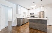 Located at 483 Valley St in Maplewood, NJ, this single-floor residence combines contemporary design with functional living spaces throughout. Rich hardwood flooring flows consistently across the living areas and bedrooms, providing a warm and cohesive aesthetic.

The kitchen stands out as a central feature, showcasing high-gloss white upper cabinetry paired with wood-grain lower cabinets and white quartz countertops. A sizeable island with pendant lighting offers additional prep space, while stainless steel appliances — including a gas range, built-in microwave, dishwasher, and refrigerator — complete the modern setup.

The living and dining areas are generously proportioned, with ceiling fans, neutral white walls, and windows that draw in natural light. One room features sliding glass doors opening to a private balcony with outdoor views of surrounding greenery.

Bedrooms are well-sized with hardwood floors, windows fitted with blinds, and ceiling-mounted lighting. Two bathrooms serve the unit: one features large-format neutral tile, a soaking tub and shower combination with a wooden vanity, while the second offers a glass-enclosed walk-in shower, tile wainscoting, and a sleek white quartz vanity. The overall ambiance is clean, modern, and move-in ready.
