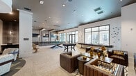 Located at 1515 Rollick Rd in Cary, NC, this single-floor community amenity space offers a generously sized, thoughtfully designed environment ideal for socializing and relaxation. The open-concept main living area features large floor-to-ceiling windows that flood the space with natural light and offer views of the surrounding community and pool area. Polished stone tile flooring, recessed lighting, and pendant fixtures contribute to the modern, upscale aesthetic throughout. A dedicated game room includes a pool table and foosball table, set beneath dramatic pendant lighting, making it a standout entertainment hub. Rich leather seating arrangements, layered rugs, and curated artwork create a sophisticated lounge atmosphere in the adjoining living area. A separate lounge zone features a flat-screen TV mounted on a textured accent wall, complemented by plush seating and bold patterned rugs. The covered outdoor terrace is equipped with ceiling fans, a linear gas fireplace set into a stacked stone wall, a wall-mounted TV, and outdoor lounge furniture on turf accents, offering a comfortable year-round retreat with views of the resort-style pool. Inside, intimate wood-paneled booth seating and a boldly patterned carpet define a lounge and co-working nook, adding a warm contrast to the brighter open areas. The overall ambiance is contemporary, inviting, and versatile.