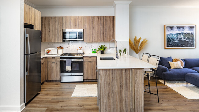 Apartment kitchen with stainless steel appliances, quartz countertops and wood-style flooring. - Griffis South Bay