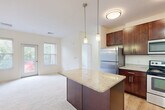This well-appointed 3-bedroom, 1-bathroom residence in Arlington, MA offers a thoughtfully designed single-floor layout. The open-concept kitchen and combined dining and living area serve as the heart of the home, creating a seamless flow for everyday living. The kitchen is outfitted with rich dark-wood cabinetry, granite countertops, stainless steel appliances including a refrigerator, range, microwave, and dishwasher, and a central island with pendant lighting overhead. Light hardwood flooring anchors the kitchen, transitioning to plush carpeting in the living and bedroom areas. Natural light fills the living space through large windows and a glass door that provides outdoor views. The generously sized primary bedroom includes its own closet with wire shelving systems for organized storage. Two additional bedrooms, each carpeted and featuring windows with outdoor views, offer comfortable and versatile spaces. The bathroom is clean and modern, featuring a floating dark-wood vanity with a white countertop, a framed mirror, and wood-look flooring. A dedicated laundry area and hallway round out the functional layout, making this residence a practical and comfortable home in a desirable Massachusetts location.