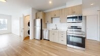 This well-designed 1-bedroom, 2-bathroom residence offers a thoughtful single-floor layout that maximizes every square foot. Light wood flooring flows throughout, creating a warm and cohesive aesthetic across all living areas.

The open-concept kitchen and living area form the heart of the home. The kitchen is outfitted with light wood cabinetry extending to the ceiling, stainless steel appliances including a refrigerator, dishwasher, range, and over-the-range microwave, complemented by a chevron-patterned white tile backsplash and light countertops. A stacked in-unit washer and dryer is conveniently tucked nearby.

The living area benefits from an expansive floor-to-ceiling window wall that floods the space with natural light and offers views of the surrounding urban streetscape.

The bedroom is a calm, bright retreat featuring multiple windows with city views and a built-in sliding-door closet. It connects directly to one of the two bathrooms, which showcases striking marble-look tile covering both the floors and full shower surround, complete with a glass-enclosed shower stall and warm wood vanity. The second bathroom provides additional convenience with matching marble-style tile flooring. Clean white walls and modern finishes throughout lend the entire space a crisp, contemporary feel.