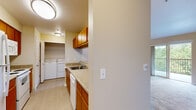 This single-floor residence offers a thoughtfully designed layout that balances functionality and comfort throughout. The spacious living area is a highlight of the home, featuring vaulted ceilings, plush wall-to-wall carpeting, and a ceiling fan. Large windows and sliding glass doors flood the space with natural light and provide direct access to a private balcony overlooking mature trees and verdant surroundings.

The kitchen is designed for practicality, featuring warm honey-toned wood cabinetry, granite-look countertops, and a full suite of white appliances including a refrigerator, dishwasher, and microwave. A breakfast bar connects the kitchen to the living area, creating an open and social atmosphere. Adjacent to the kitchen is a dedicated in-unit laundry area, complete with a full-size washer and dryer and overhead wire shelving for additional storage.

The bedrooms are carpeted and generously sized, each offering ample closet space and windows with views of the surrounding greenery. The bathroom features a wide floating wood vanity with substantial drawer storage, a light countertop, a large mirror, and bright vanity lighting above. Neutral warm-toned walls and light flooring throughout lend the space a cohesive, welcoming ambiance.