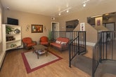 Located at 900 Country Club Dr SE in Rio Rancho, New Mexico, this single-floor community amenity space offers residents two distinct functional areas designed for relaxation and active living. The lounge area is bright and inviting, featuring warm hardwood-style flooring, large grid-pane windows that flood the room with natural light and provide views of the outdoor pool area. Comfortable wicker furnishings with rust-toned cushions, a glass-top coffee table, open shelving with decorative accents, and wall-mounted artwork create a casual yet welcoming atmosphere. The space also features a railing-lined overlook that connects to adjoining areas, adding an open, airy quality to the layout. The fitness center is a well-appointed workout space finished with durable carpet tile flooring and equipped with a variety of exercise machines, including a treadmill, elliptical, rowing machine, multi-station cable gym, and additional strength equipment. Floor-to-ceiling mirrors along one wall visually expand the room, while overhead fluorescent lighting ensures a well-lit environment. A secondary fitness area provides additional space for strength training with its own multi-function gym unit and natural light from a grid-pane window. Together, these amenities offer a functional and comfortable environment for the residents of this Rio Rancho community.
