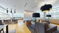 Located at 340 E North Water Street in Chicago's prestigious Streeterville neighborhood, this single-floor amenity lounge is a masterfully designed social and recreational space. The open-plan layout is anchored by warm herringbone hardwood flooring that runs throughout, complemented by crisp white ceilings with recessed and linear lighting accented by striking black-and-gold drum pendant and floor lamps.

The lounge is organized into distinct yet interconnected zones. A generous seating area features plush gray tufted sofas and earthy brown accent chairs arranged around glass coffee tables atop a geometric area rug, ideal for gathering and conversation. Adjacent to this, a full media wall clad in rich warm wood paneling houses a large flat-screen television flanked by built-in cabinetry, creating a refined entertainment focal point.

A billiards area occupies a sun-drenched corner, bathed in natural light from floor-to-ceiling wraparound windows that frame panoramic views of the Chicago skyline. A built-in bench seat with plush cushions lines the window wall, offering a relaxed vantage point. A bold stone-clad bar counter anchors the entertaining zone, with direct access to an outdoor terrace. The abundance of natural light and expansive city views throughout give the space a bright, urban, and distinctly upscale character.
