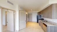 This single-floor unit offers a clean, contemporary design throughout, finished with light-toned ceramic tile flooring that unifies the entire space. The open-concept kitchen is a standout feature, showcasing warm wood-grain cabinetry extending floor to ceiling, granite-look countertops, a subway tile backsplash, and a full suite of stainless steel appliances including a range, over-the-range microwave, dishwasher, and refrigerator. A double stainless steel sink adds both function and style to the well-appointed kitchen layout.

The kitchen flows seamlessly into the living area, which benefits from abundant natural light through large sliding glass doors that open to a private balcony, offering views of the surrounding neighborhood. A ceiling fan keeps the space comfortable and airy.

The bedroom is a bright, tranquil retreat with a ceiling fan and a generously sized window that invites natural daylight. The room provides a calm atmosphere with neutral walls and the same consistent tile flooring found throughout the unit.

The bathroom is thoughtfully designed with accessibility in mind, featuring grab bars along the soaker tub and shower combination, a floating wood-grain vanity with an undermount sink, a large wall mirror, and white tile surround. An entryway with louvered closet doors and additional storage rounds out this well-designed and functional space.