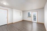 This single-floor unit features a thoughtfully designed layout that balances open communal areas with functional private spaces. The main living area is spacious and bright, finished with durable dark hardwood-style flooring and neutral-toned walls. A door leads directly to a private balcony, allowing natural light to fill the room and providing outdoor views of the surrounding neighborhood.

The entry area connects seamlessly to the living space via light hardwood-style flooring, and a pass-through window opens into the kitchen, enhancing the sense of openness. The galley-style kitchen is well-appointed with dark wood cabinetry, light countertops, stainless steel appliances including a refrigerator and microwave, and a single-basin sink — offering efficient use of the available space.

The bedroom is carpeted for comfort and features a window with blinds that frames views of surrounding greenery, allowing for ample natural light. The bathroom is finished with warm wood-tone flooring, a dark wood vanity with drawers, brushed nickel hardware, a white countertop with an integrated sink, a large mirror, and standard fixtures — presenting a clean, modern aesthetic throughout.