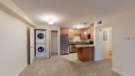 This single-floor residence at Markwell Village offers a functional and comfortable layout designed with practical living in mind. The kitchen is a standout feature, outfitted with a full suite of stainless steel appliances — including a refrigerator, range, microwave, and dishwasher — complemented by warm honey-toned cabinetry, granite-style countertops, and a peninsula that provides additional prep space and seating. Light tile flooring runs throughout the kitchen, creating a clean and easy-to-maintain surface. Conveniently adjacent to the kitchen is an in-unit laundry area housing a stacked washer and dryer, along with a walk-in closet for additional storage. The bathroom features full tile surround on the shower-tub combination, tile flooring, and classic brushed nickel fixtures, lending a clean, polished look. The living area is generously proportioned with soft carpeting underfoot and a window fitted with blinds that allows natural light to fill the space. The bedroom is equally well-sized, with plush carpeting and a window overlooking the surrounding neighborhood. Neutral wall tones throughout the residence create a versatile backdrop, and the single-story layout ensures a seamless, accessible flow from room to room.