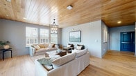 Located at 6163 Kempsville Circle in Norfolk, Virginia, this thoughtfully designed single-floor space blends contemporary style with warm, natural materials throughout. The standout architectural feature is the striking tongue-and-groove wood plank ceiling that spans the living area, adding texture, warmth, and a sense of elevated character to the interior.

The living room is bright and welcoming, with a generous arrangement of windows that flood the space with natural light and offer outdoor views. Light hardwood floors run throughout, complementing the warm ceiling tones. A statement wrought-iron chandelier anchors the room, while soft, neutral furnishings create a relaxed yet refined atmosphere. A door provides direct access to an outdoor area, enhancing the connection between interior and exterior.

The dining room offers a more intimate setting, distinguished by classic shiplap-style wainscoting and board-and-batten wall detailing finished in crisp white. A pendant light fixture hangs over the central dining area, and a window allows natural light to filter in. The overall aesthetic is clean and timeless.

Connecting the two spaces is a well-proportioned hallway with a dramatic arched steel-framed mirror and continued wood ceiling detail, contributing to the cohesive design language that runs throughout this refined and carefully curated space.