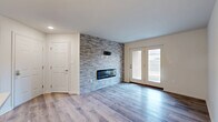 Located in Miamisburg, Ohio, this well-appointed single-floor, one-bedroom, one-bathroom home offers a modern aesthetic combined with functional design throughout. The living room serves as a standout centerpiece, showcasing a full-wall stacked stone accent with a sleek linear electric fireplace and light hardwood-style flooring that extends throughout the main living areas. French doors off the living room invite natural light and provide direct access to the private patio, creating a seamless indoor-outdoor connection. The open kitchen is equipped with rich dark-espresso cabinetry, stainless steel appliances including a refrigerator, range, and microwave, white quartz countertops, and a peninsula with an undermount sink and pendant lighting overhead — ideal for both meal prep and casual dining. The adjacent dining area flows naturally from the kitchen. The spacious bedroom features plush carpeting, a ceiling fan with light fixture, a generous closet with built-in shelving, and a window with outdoor views. The bathroom offers a glass-enclosed walk-in shower with marble-style tile surround and wood-look flooring. Additional highlights include four closets, in-unit laundry, and a hallway connecting all spaces efficiently.