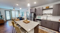 Located at 10387 Vista Oaks Ct in Orlando, FL, this well-appointed single-floor residence offers a thoughtfully designed open-concept layout. The kitchen serves as the heart of the home, showcasing rich gray wood-grain cabinetry, granite countertops, a subway tile backsplash, and a full suite of stainless steel appliances including a refrigerator, range, microwave, and dishwasher. A generously sized granite-topped island with bar seating and pendant lighting above creates a natural gathering space that flows seamlessly into the living area. The living room benefits from abundant natural light through large windows with custom drapery, and provides access to an exterior door. Warm wood-look flooring runs throughout the main living areas, adding cohesion and style. The bedrooms are carpeted for comfort, each featuring ceiling fans and windows that bring in natural light. The primary bathroom is well-sized, offering a granite vanity with dark wood cabinetry, wood-look flooring, a tub-shower combination with tile surround, and direct access to a spacious walk-in closet. A secondary bathroom mirrors the same refined finishes. Throughout the residence, a clean, contemporary aesthetic with neutral tones and modern fixtures creates a welcoming and functional living environment.