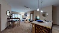 Located in Beavercreek, Ohio, this single-floor residence offers a thoughtfully designed open-concept layout that seamlessly connects the kitchen, dining, and living areas. The kitchen is a functional centerpiece, showcasing dark espresso cabinetry, black appliances, a granite-topped island with bar seating, pendant lighting, and track lighting overhead — all set on large-format tile flooring. The open living and dining space transitions to plush carpeting, creating a comfortable and inviting atmosphere. The living room is bright and airy, highlighted by a sliding glass door that opens to a private balcony with outdoor views, allowing natural light to fill the space. Two generously sized bedrooms feature carpet flooring, ceiling fans, and multiple windows dressed with horizontal blinds for light control. Each bedroom includes walk-in closet space with built-in shelving and hanging rods. The bathrooms are appointed with large-format tile floors, dark vanity cabinetry, white countertops, and well-lit mirrors. A dedicated laundry area and additional storage add practical convenience. Throughout the residence, neutral warm tones, panel-style interior doors, and consistent finishes contribute to a cohesive and modern aesthetic.