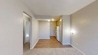 This two-bedroom, one-bathroom unit offers a practical and efficient single-floor layout designed to maximize functionality within a compact footprint. The combined kitchen and living area serves as the heart of the home, where light-toned hardwood-style flooring transitions seamlessly into carpeted living space. The kitchen is equipped with white appliances — including a refrigerator and range — paired with warm-toned cabinetry, while a window unit provides climate control in the living area. Natural light filters in through blinds-covered windows, lending a bright and airy feel throughout. A hallway connects the main living space to the private areas of the unit, leading to two carpeted bedrooms, each featuring neutral gray walls and dedicated closet space. The primary bedroom is a comfortable size, receiving natural light through a window. The second bedroom offers similar finishes and a bright atmosphere. The shared full bathroom is clean and straightforward, featuring a tiled tub-shower combination with a curtain and standard white fixtures. Textured ceilings are consistent throughout, and the overall color palette of soft grays and warm neutrals creates a calm, cohesive ambiance well-suited for everyday living.