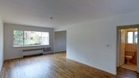 Located at 41 Wolfpit Ave in Norwalk, Connecticut, this single-floor residence offers a straightforward and functional layout designed for comfortable everyday living. The main living area is a standout feature, showcasing warm hardwood floors that run throughout the space, contributing to a bright and inviting atmosphere. Crisp white walls provide a clean, neutral backdrop that enhances the sense of openness throughout the room. A large picture window allows abundant natural light to fill the living area, offering views of the surrounding greenery outside. The window is complemented by a baseboard heating unit and a wall-mounted air conditioning unit, ensuring year-round climate comfort. The open wall space provides flexibility for a variety of furniture arrangements, making the living area highly adaptable. A doorway visible from the main room leads further into the unit, suggesting additional living or storage space. The overall ambiance of the space is clean, airy, and understated, appealing to those who value simplicity and practicality. Situated in the Wolfpit neighborhood of Norwalk, CT, the property benefits from its established residential surroundings, offering a quiet and convenient setting.