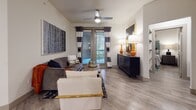 This single-story residence is designed with a modern aesthetic, combining functional layouts with contemporary finishes throughout. Wood-look plank flooring flows consistently across all rooms, providing a cohesive and clean foundation for the space.

The living area serves as the central gathering space, featuring a ceiling fan, a large sliding glass door that allows natural light and outdoor views, and neutral walls accented by bold décor. The open layout connects seamlessly to the kitchen and dining area.

The kitchen is well-appointed with dark espresso cabinetry, stainless steel appliances including a refrigerator, microwave, and range, and a generous granite-topped island with bar seating. Globe pendant lights hang above the island, adding a modern touch. An adjacent dining area provides additional seating space.

Multiple bedrooms are present, each equipped with a ceiling fan, window with blinds and decorative curtains, and ample room for full-size furniture. The rooms maintain the same wood-look flooring and neutral wall tones seen throughout the residence.

The bathroom features a walk-in glass-door shower, wood-look flooring, and a clean, minimalist design. Overall, the space presents a well-balanced combination of practical design and modern style.