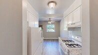 Located at 1717 Bath Rd in Bristol, PA, this one-bedroom, one-bathroom unit offers a practical and well-appointed single-floor layout. Light wood-style flooring runs throughout, complementing the neutral gray walls and white trim that give the space a clean, cohesive feel. The galley-style kitchen flows directly into the dining area and features white cabinetry with granite-look countertops, a gas range, and a full-size refrigerator, all illuminated by a flush ceiling light. The adjoining living and dining area is bright and open, benefiting from multiple windows that frame lush, green outdoor views, with a ceiling fan and baseboard heating ensuring year-round comfort. The spacious primary bedroom includes its own window with natural light, a closet with built-in shelving, and the same hardwood-style flooring found throughout. A second closet provides additional storage. The bathroom is notably updated, featuring large marble-style wall and floor tiles, a white vanity, and a window for natural ventilation. Two hallways connect the rooms efficiently, rounding out a functional and well-maintained living space.