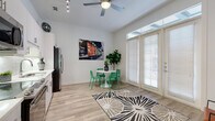 Located at 6125 Via la Cantera in the northwest San Antonio community of 78256, this efficiently designed single-floor residence makes excellent use of its intimate footprint. The open-concept kitchen and living area serves as the heart of the home, featuring sleek white cabinetry, a classic subway tile backsplash, stainless steel appliances including a French door refrigerator, microwave, range, and dishwasher, all set atop warm wood-look flooring. Track lighting and a ceiling fan overhead enhance both functionality and comfort. A wall of floor-to-ceiling French doors with transom windows floods the living space with abundant natural light and provides direct access to a private patio, creating a seamless indoor-outdoor flow. The bedroom offers plush carpeting and a high horizontal clerestory window that introduces additional natural light while maintaining privacy. Two full bathrooms, a dedicated utility room, in-unit laundry, a hallway, and a closet round out the well-organized layout. The overall design palette is clean and modern, with crisp white walls and thoughtful architectural details that maximize the sense of openness throughout the space.