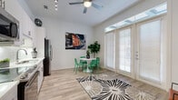 Located at 6125 Via la Cantera in the northwest San Antonio community of 78256, this efficiently designed single-floor residence makes excellent use of its intimate footprint. The open-concept kitchen and living area serves as the heart of the home, featuring sleek white cabinetry, a classic subway tile backsplash, stainless steel appliances including a French door refrigerator, microwave, range, and dishwasher, all set atop warm wood-look flooring. Track lighting and a ceiling fan overhead enhance both functionality and comfort. A wall of floor-to-ceiling French doors with transom windows floods the living space with abundant natural light and provides direct access to a private patio, creating a seamless indoor-outdoor flow. The bedroom offers plush carpeting and a high horizontal clerestory window that introduces additional natural light while maintaining privacy. Two full bathrooms, a dedicated utility room, in-unit laundry, a hallway, and a closet round out the well-organized layout. The overall design palette is clean and modern, with crisp white walls and thoughtful architectural details that maximize the sense of openness throughout the space.