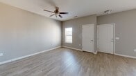 This 910 square foot single-story residence offers a well-designed layout with two bedrooms and an open-concept living area. The home features a modern aesthetic with neutral gray walls and wood-look flooring throughout, creating a cohesive and contemporary ambiance.

The primary bedroom, measuring 140 square feet, provides ample space and includes a ceiling fan for added comfort. Both bedrooms feature windows that allow natural light to filter in, brightening the spaces. The open-concept living area seamlessly combines the kitchen and living room, promoting a spacious feel and facilitating easy interaction between spaces.

The kitchen boasts dark wood cabinetry contrasting nicely with light-colored countertops, and is equipped with modern black appliances. Pendant lighting over the kitchen area adds a touch of style and functionality. The living room area is illuminated by large windows and a central lighting fixture, creating a welcoming atmosphere for relaxation or entertainment.

Throughout the home, white two-panel doors and baseboards provide a clean, crisp look that complements the overall design. Ceiling fans in various rooms offer both style and practicality. The property's efficient use of space and contemporary finishes make it an attractive option for those seeking a modern, low-maintenance living environment.